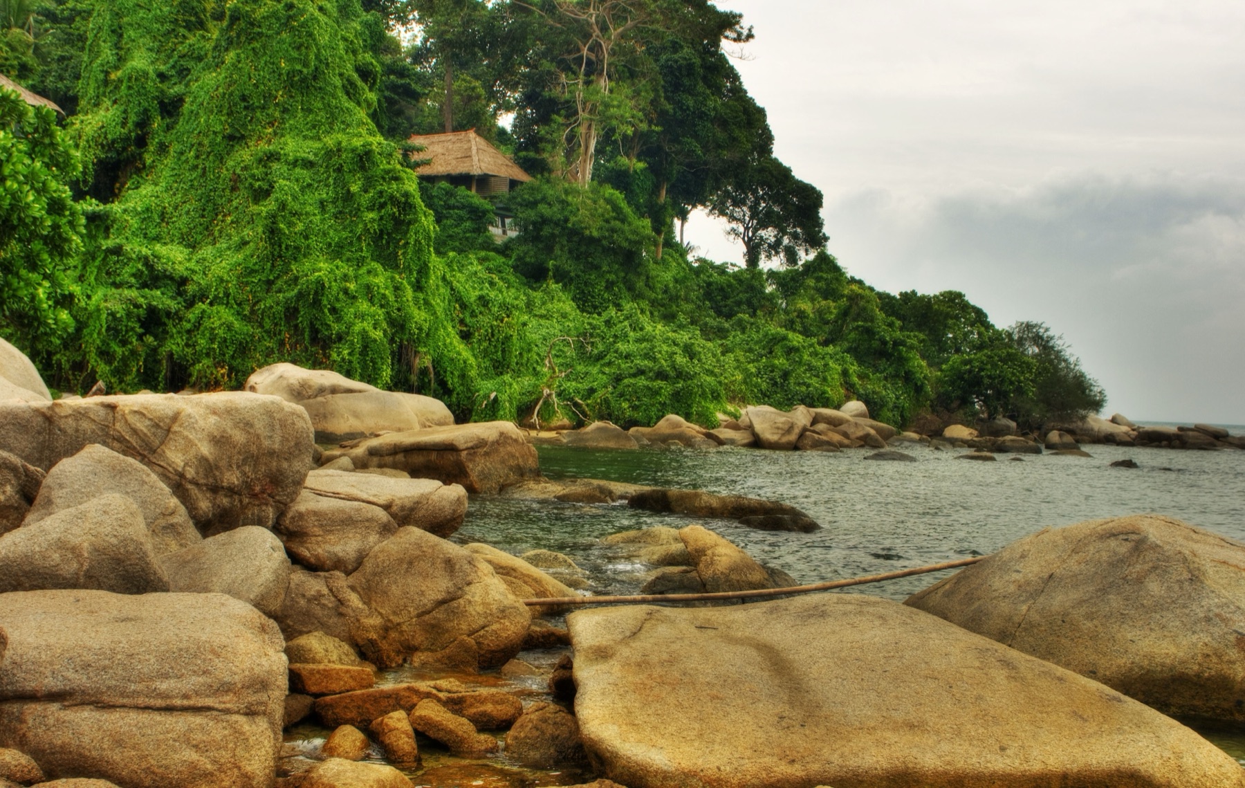 Granite boulder coastline with jungle canopy and a villa roof at Banyan Tree Bintan.
