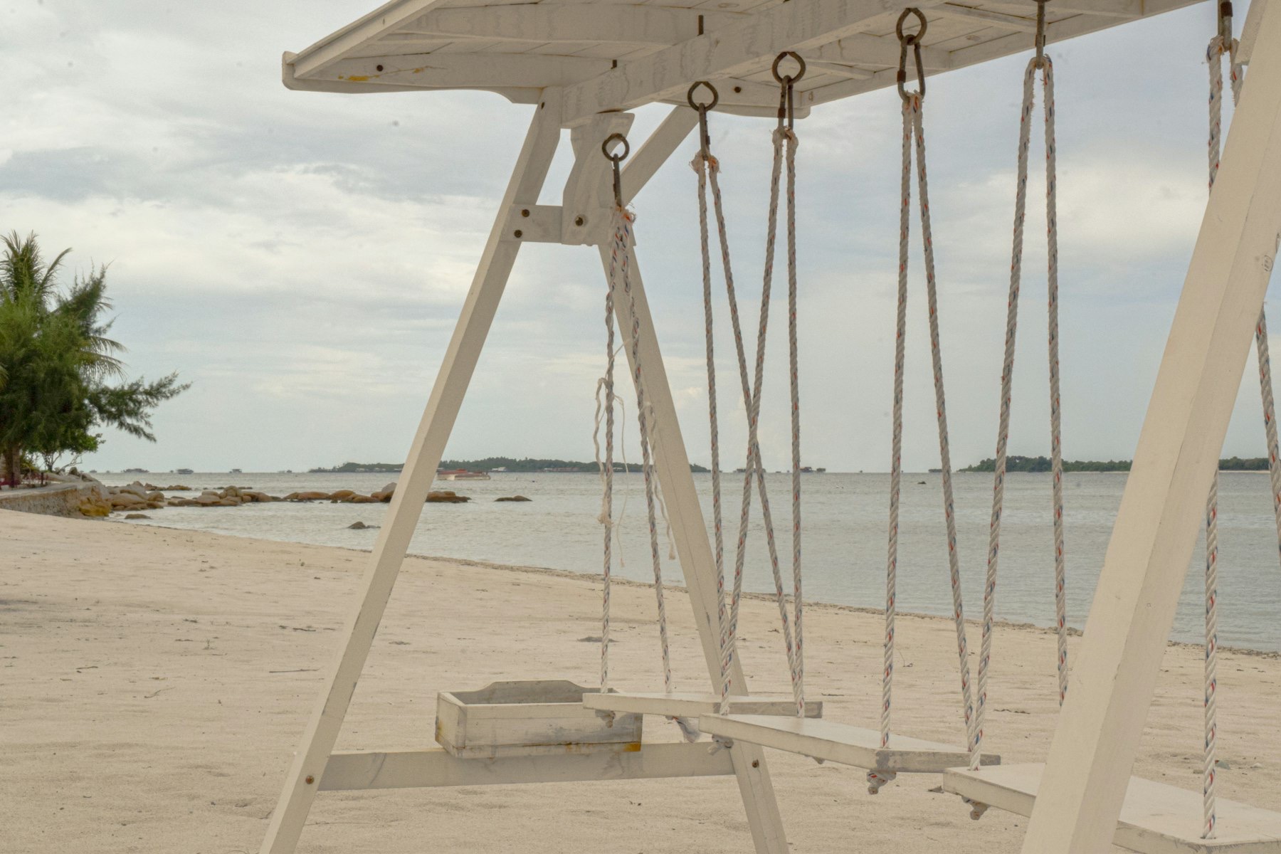A white rope swing standing in shallow turquoise water off a Riau Islands beach.