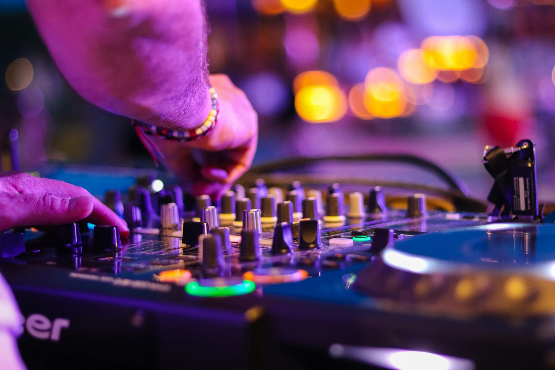 A DJ’s hands on mixing decks lit in neon at night.