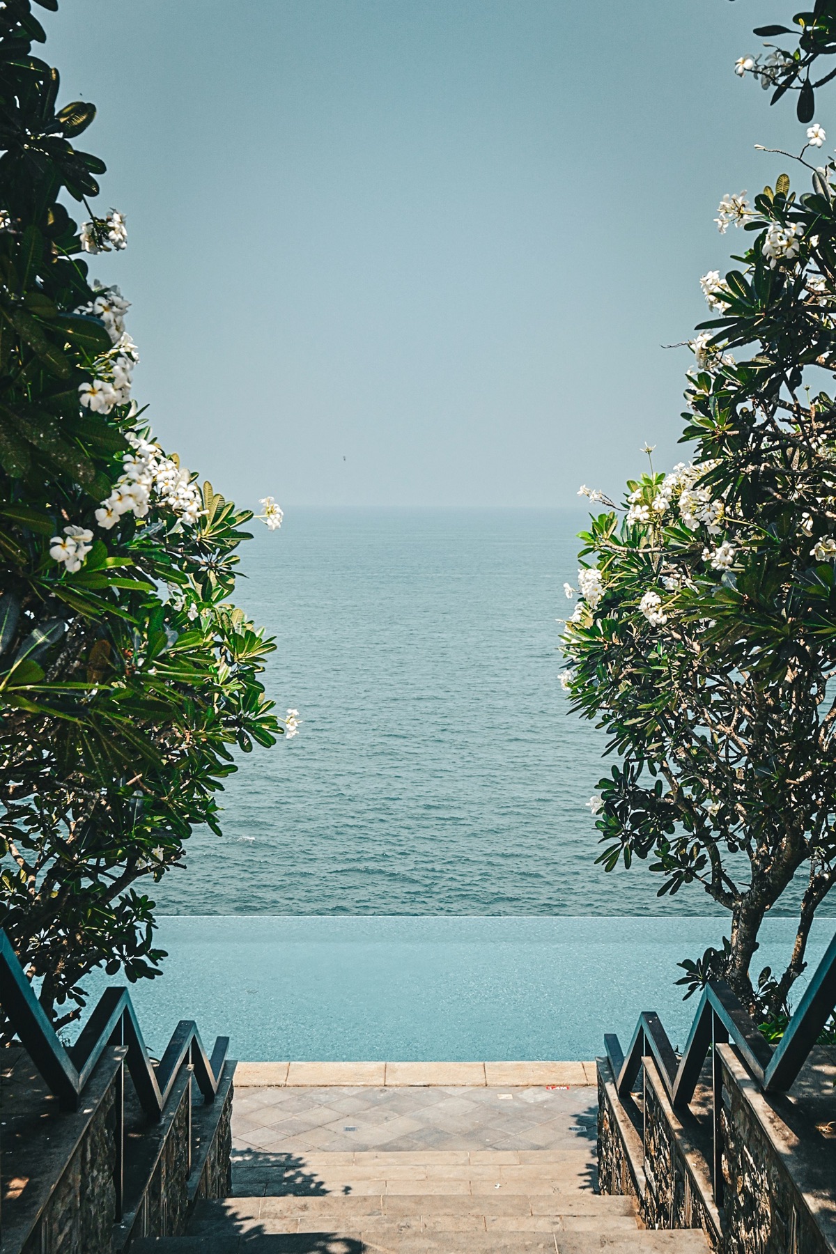 Frangipani-lined stone steps descending to an ocean-view pool and spa deck.